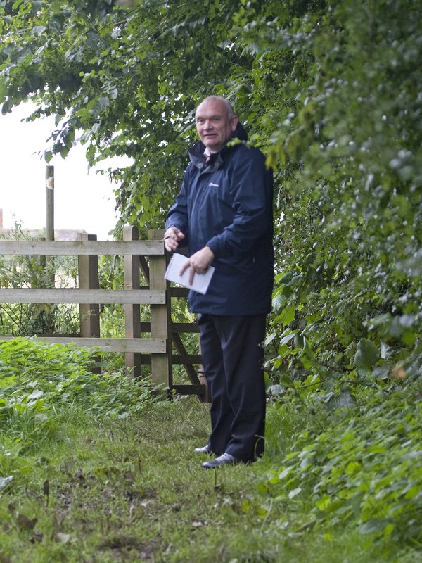 A council officer standing on the track at Lucies Farm beside a wooden gate, papers in his hand